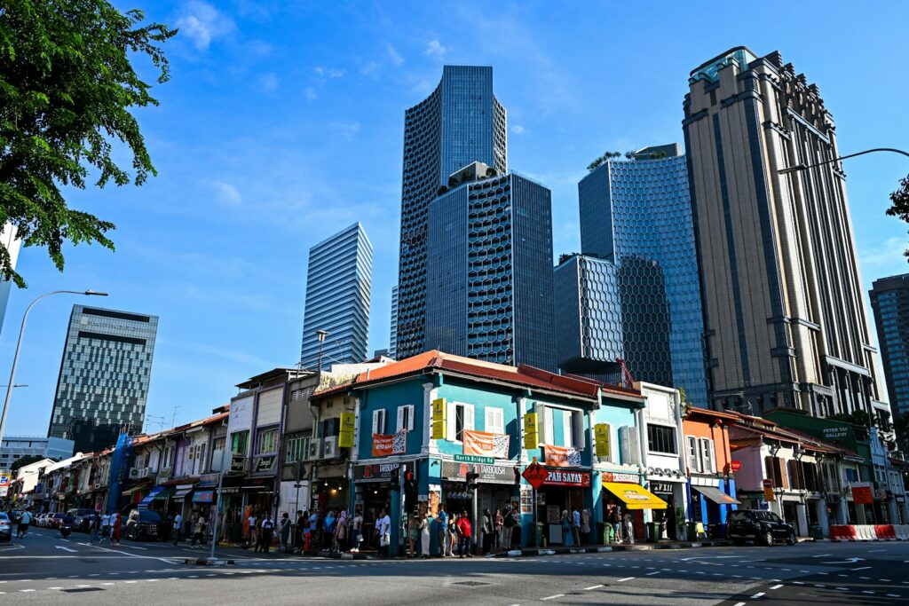 Colorful shophouses against modern skyscrapers under blue sky.